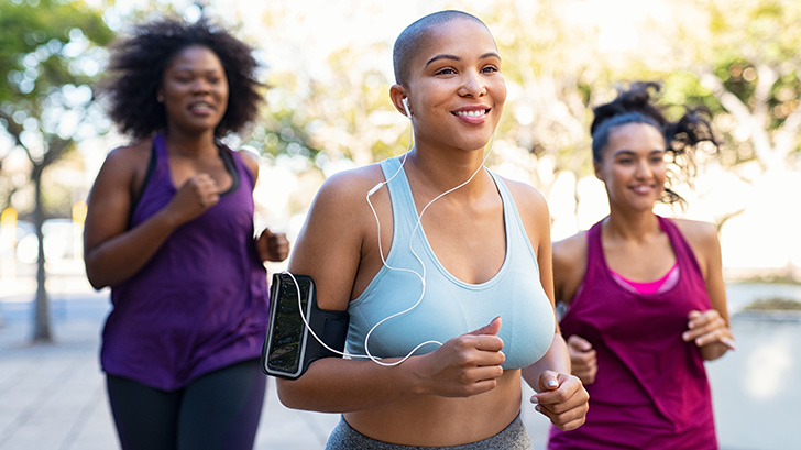 Three women outside in workout clothes, jogging and smiling.