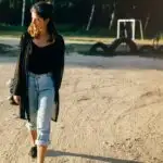 Woman wearing boyfriend jeans outfit outside, walking on dirt road.