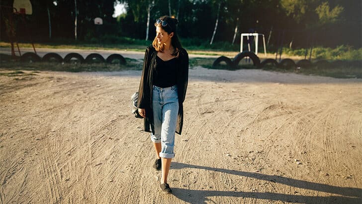 Woman wearing boyfriend jeans outfit outside, walking on dirt road.