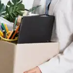 Woman carries personal items out of office after getting laid off.