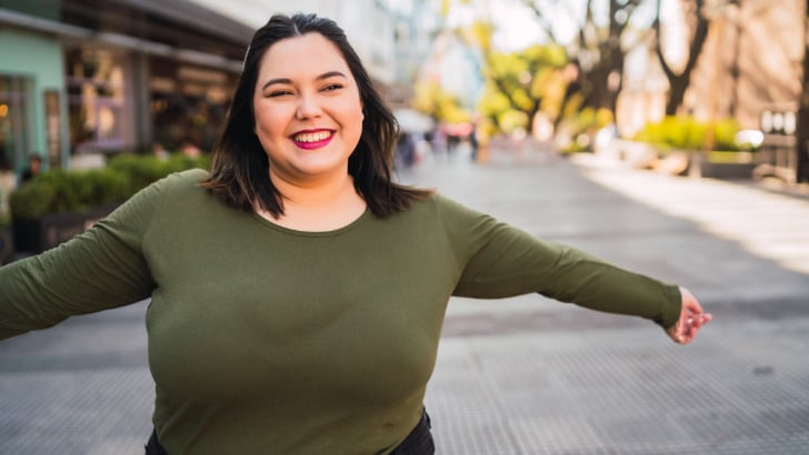 Woman with large bust smiles outside.