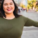 Woman with large bust smiles outside.