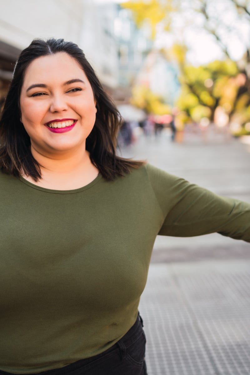 Woman with large bust smiles outside.