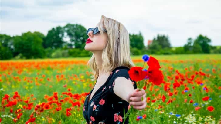 Woman wearing summer dress style stands in filed of flowers.