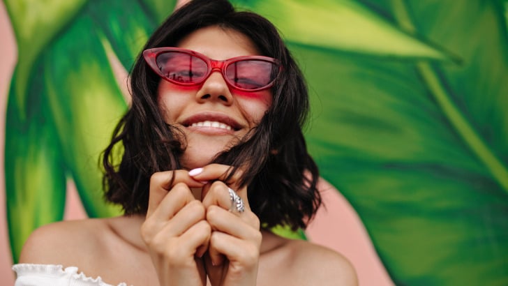 Woman smiles while wearing pink cat-eye sunglasses.