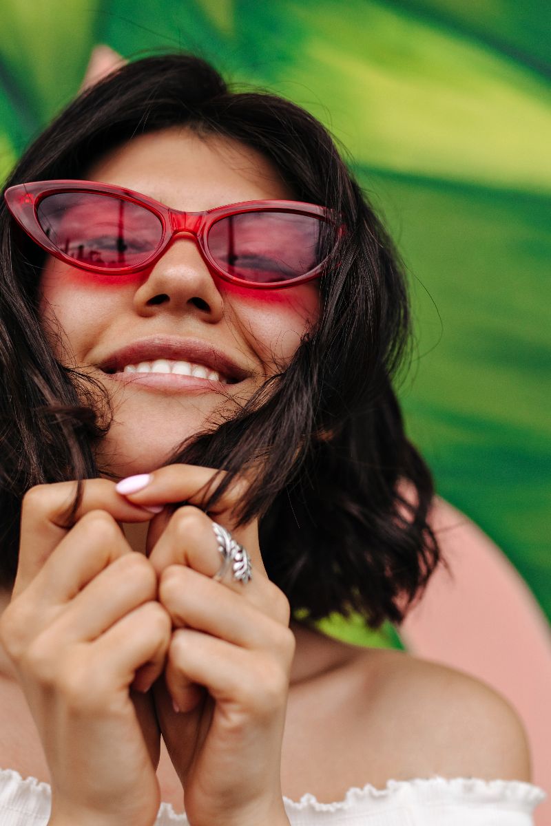Woman smiles while wearing pink cat-eye sunglasses.