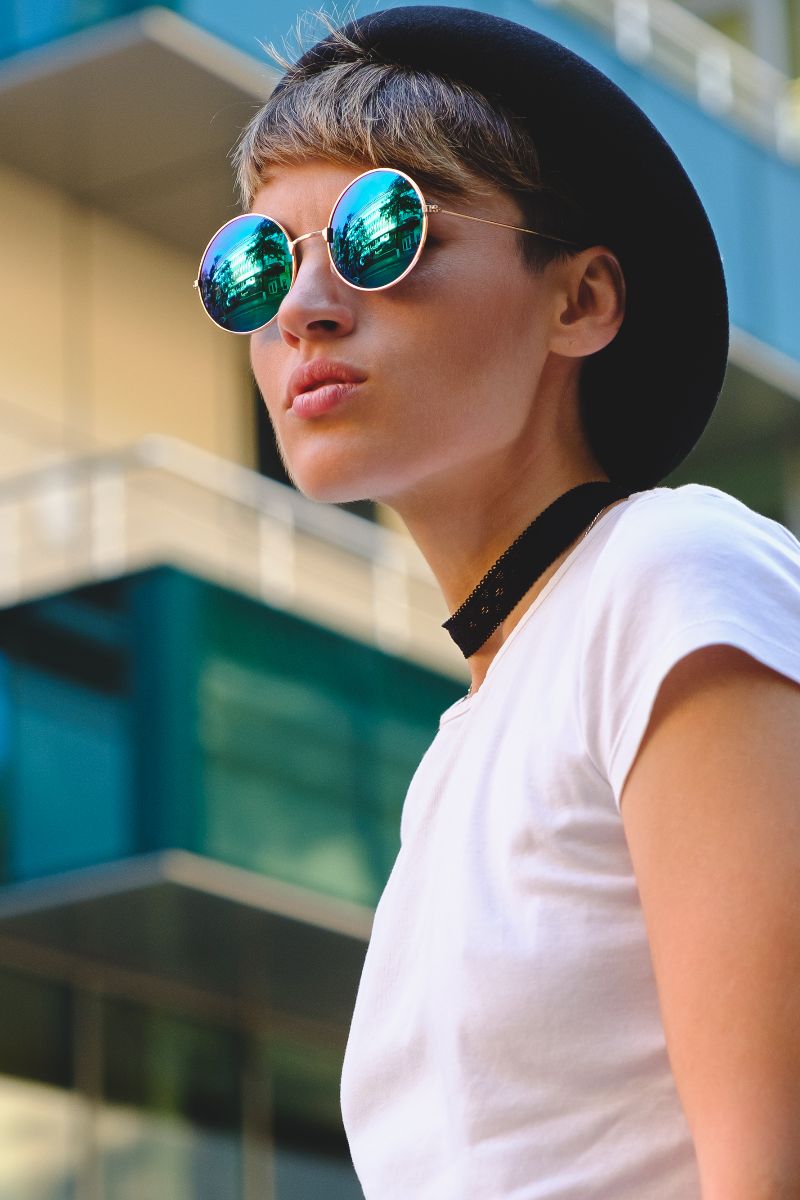 Side view of woman wearing round sunglasses and hat. 