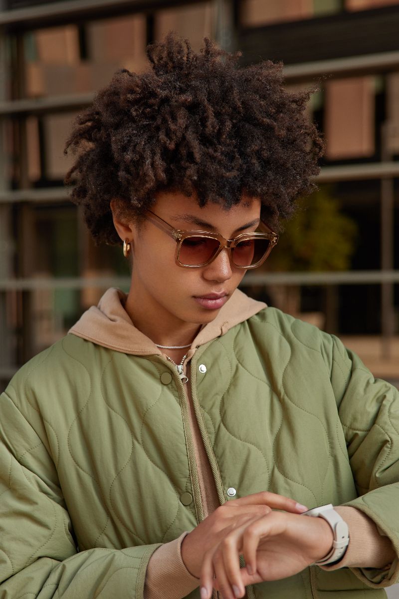 Woman wearing color-coordinated sunglasses looks at her watch.