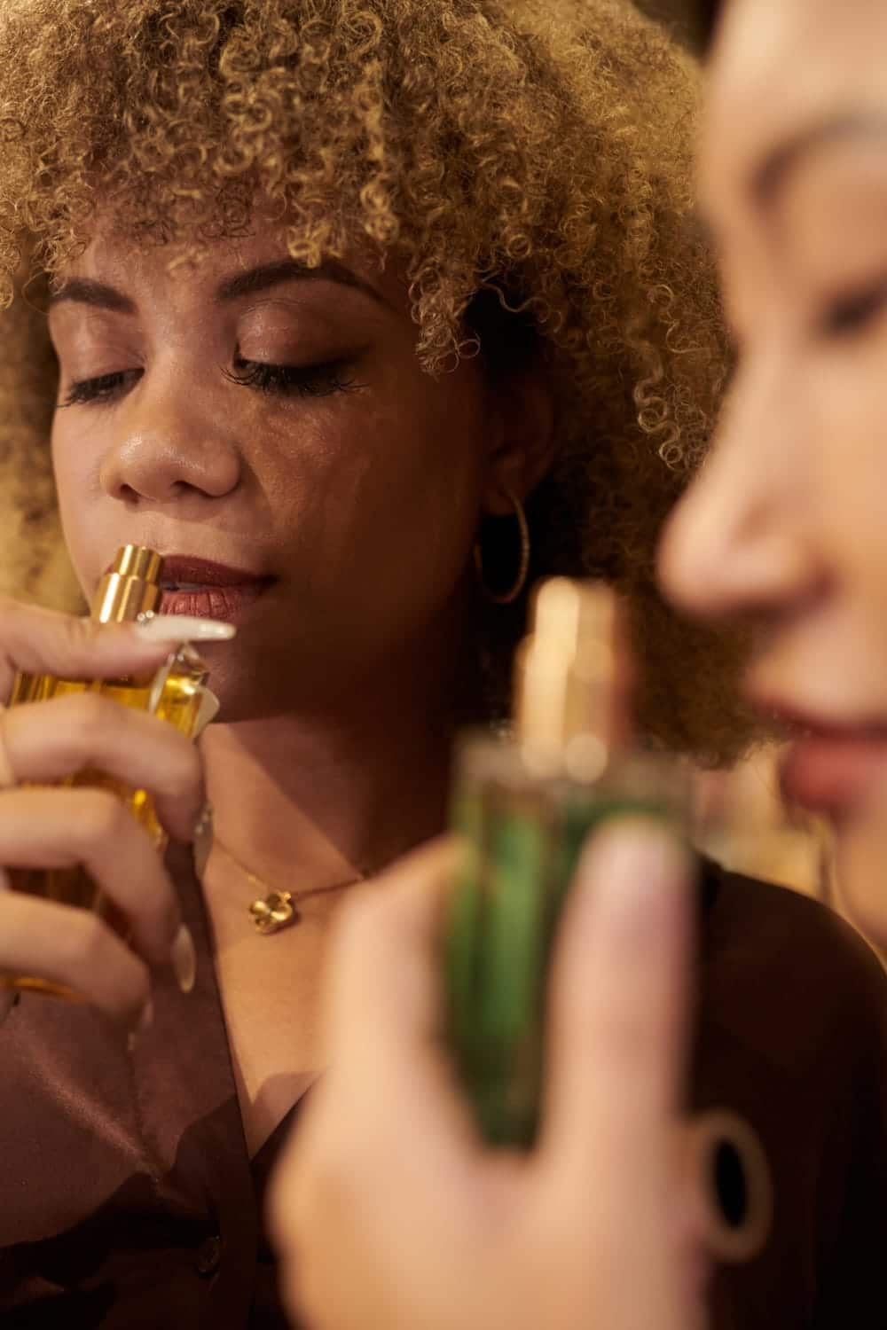 Two women smell body mists with their eyes closed.
