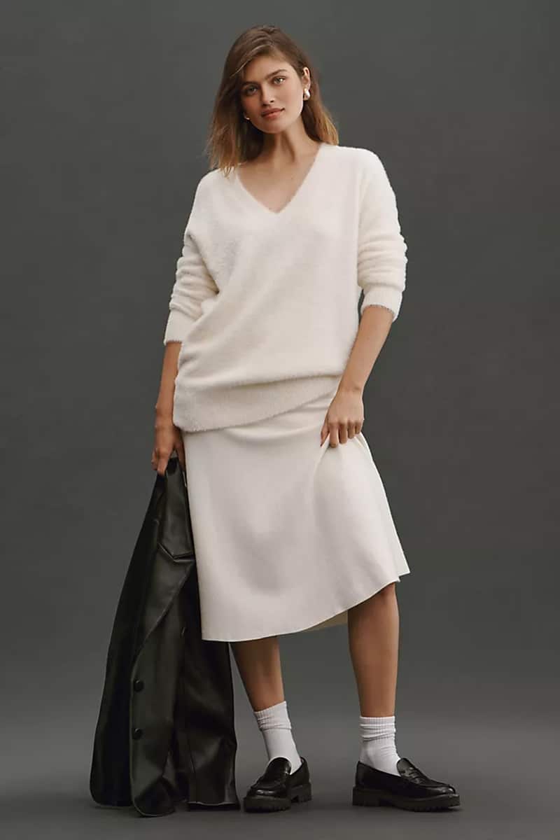 Model wears v-neck top with midi skirt and holds jacket. 