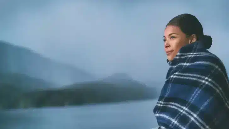 Woman standing on cruise ship deck wrapped in blanket to represent dry skin and travel.