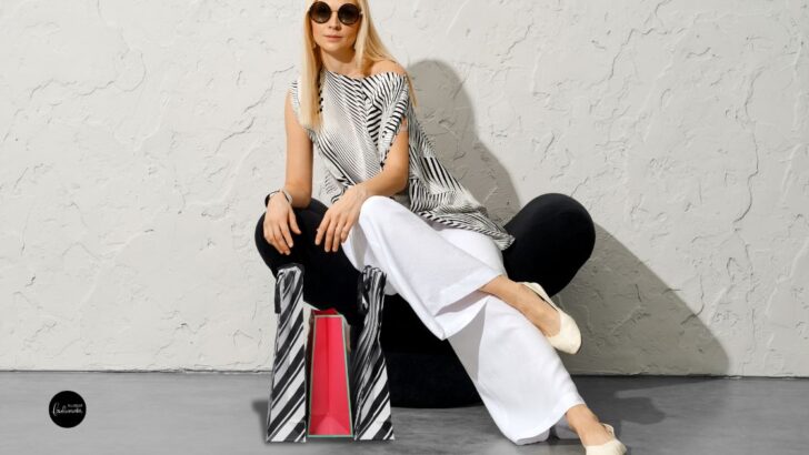 Woman sitting wearing wide-legged pants with a striped bag.