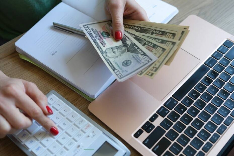 Hand holding cash over laptop to represent stagflation and inflation