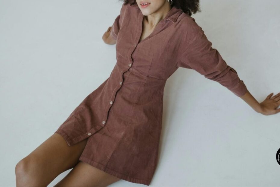 Woman wearing brown shirt dress leaning against white wall